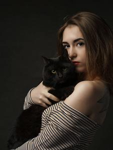 美丽性感的黑衣女人抱着黑猫.美丽的年轻时尚的女人抱着一只灰色的猫.